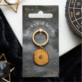 Gold astrological keyring on a branded card with decorative items around
