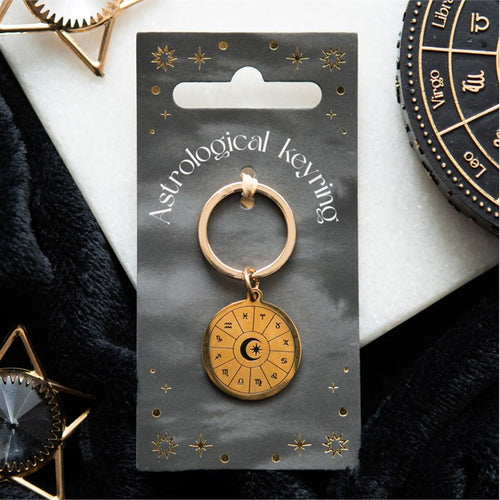 Gold astrological keyring on a branded card with decorative items around