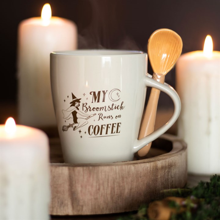 White mug with 'My Broomstick Runs on Coffee' text, wooden spoon, and candles in the background