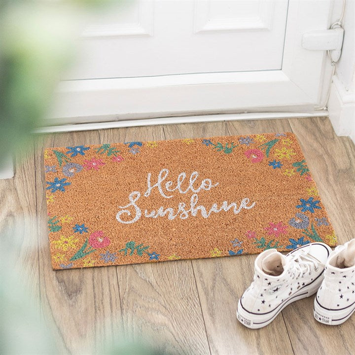 Doormat with 'Hello Sunshine' text and floral designs on a wooden floor.