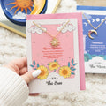 Necklace with sun charm on a card held by a hand, with other jewelry items in the background.