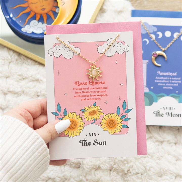Necklace with sun charm on a card held by a hand, with other jewelry items in the background.