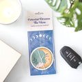 Celestial Dreams The Moon vanilla scented air freshener packaging on a white surface with a car key and plant in the background.