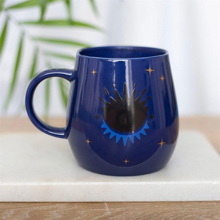 Blue mug with star and moon design on a white surface with a plant in the background