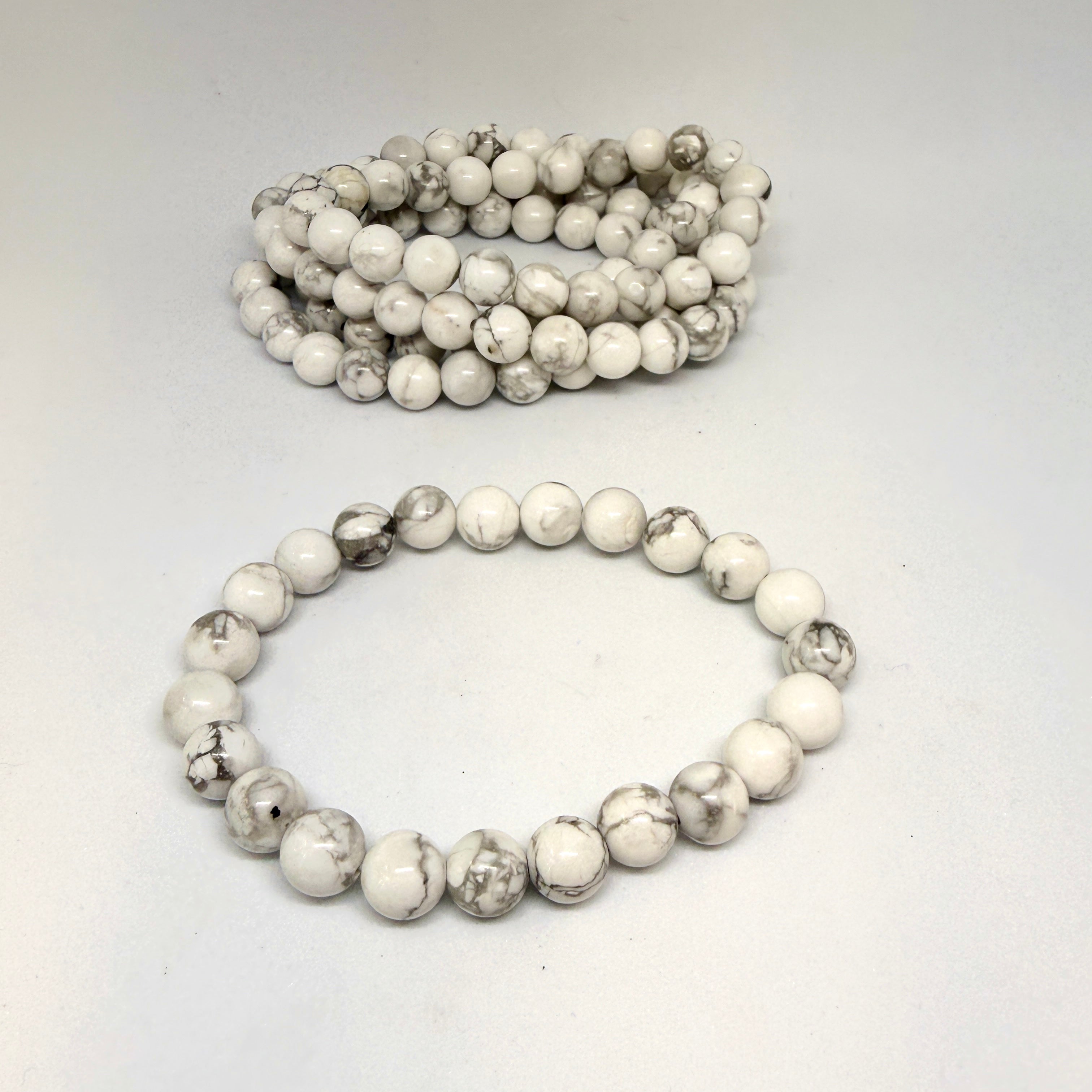 Two white beaded bracelets on a light gray background
