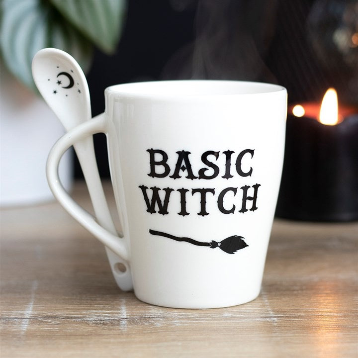 White mug with 'BASIC WITCH' text on a wooden surface with a blurred candle in the background
