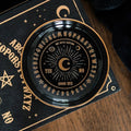 Decorative black and gold circular object with symbols on a wooden surface
