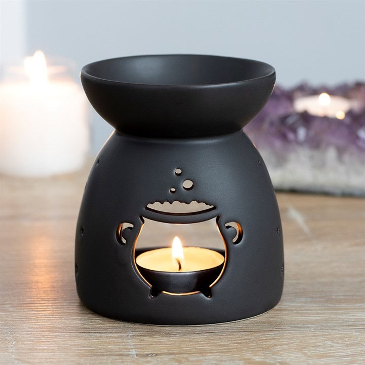 Black ceramic cauldron oil burner lit with fragrance oil in home setting
