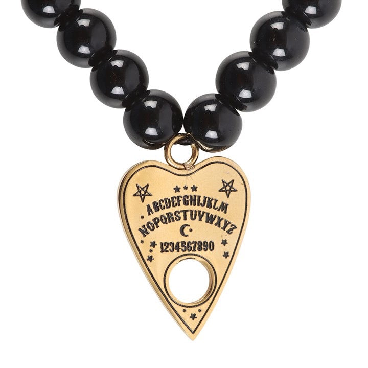 Black beaded bracelet with a gold heart-shaped Ouija board charm on a white background