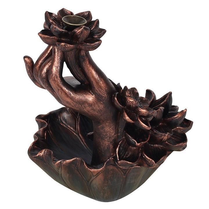 Bronze-colored incense burner shaped like a hand holding a lotus flower on a white background