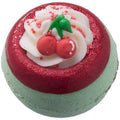Bath bomb with red and green top, white cream, and cherry decoration on a white background