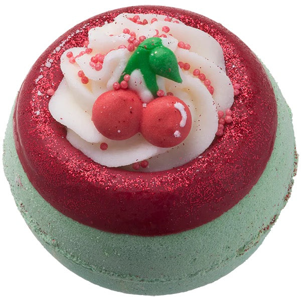 Bath bomb with red and green top, white cream, and cherry decoration on a white background