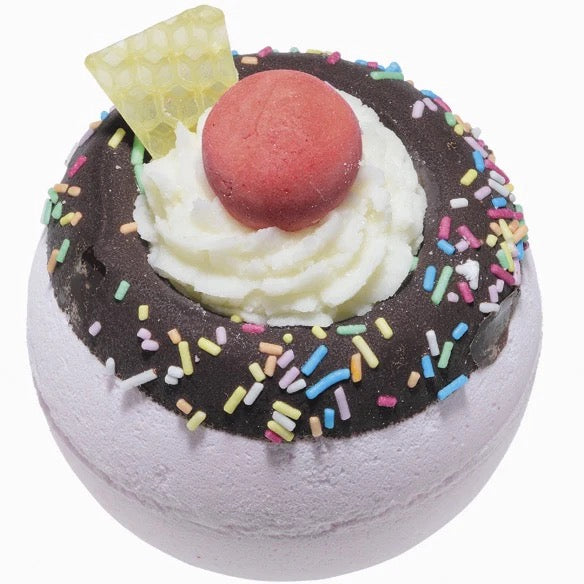 Bath bomb with chocolate topping, whipped cream, and colorful sprinkles on a white background
