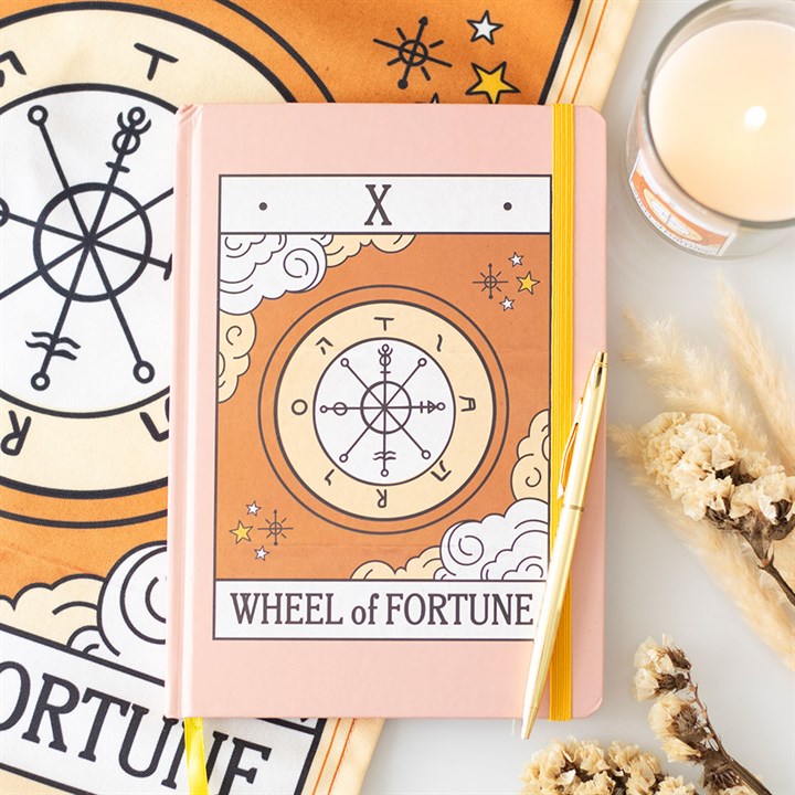 Notebook with 'Wheel of Fortune' design on a table with tarot cards and candles.
