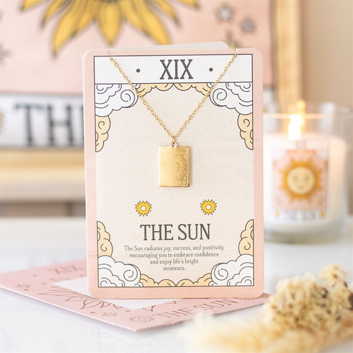 Necklace with a gold pendant on a decorative card with 'The Sun' theme, placed on a surface with a blurred background.