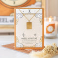 Gold necklace with 'Wheel of Fortune' pendant on a decorative card, with a blurred background.