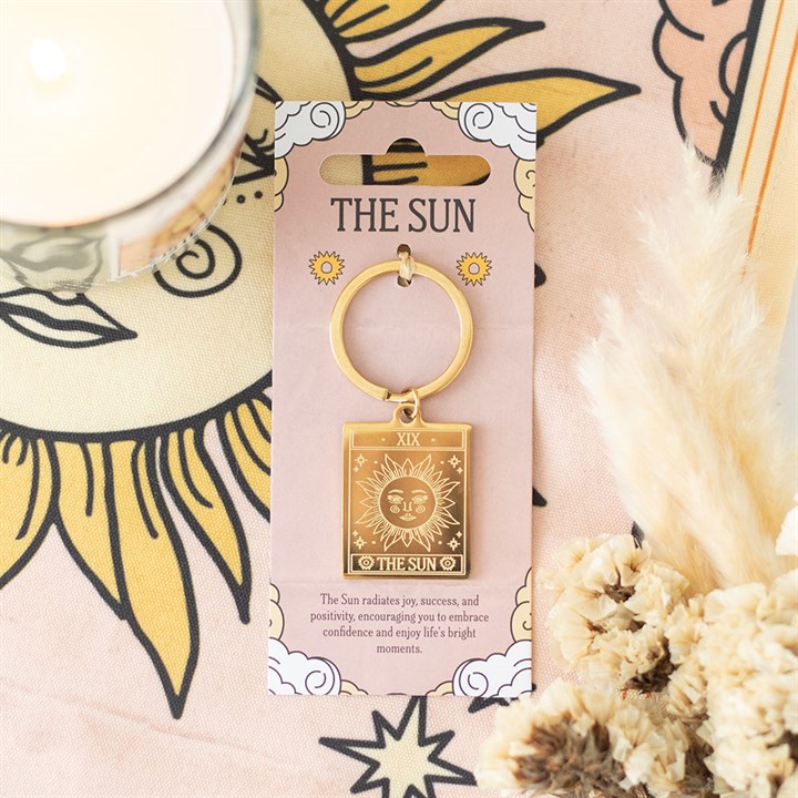 Gold keychain with 'The Sun' design on a pink card, surrounded by decorative elements.