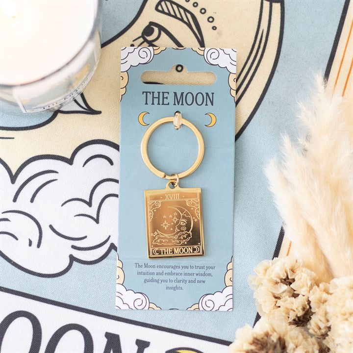 Gold keychain with 'The Moon' card design on a blue card, with decorative elements in the background.