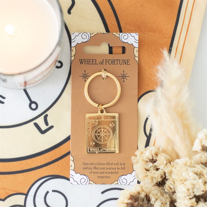 Gold 'Wheel of Fortune' keychain on a decorative card with a clock and dried plants in the background.