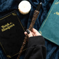 Hand holding a wooden wand with books and a candle on a dark fabric background