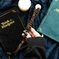 Hand holding a decorative wand with books and a candle in the background