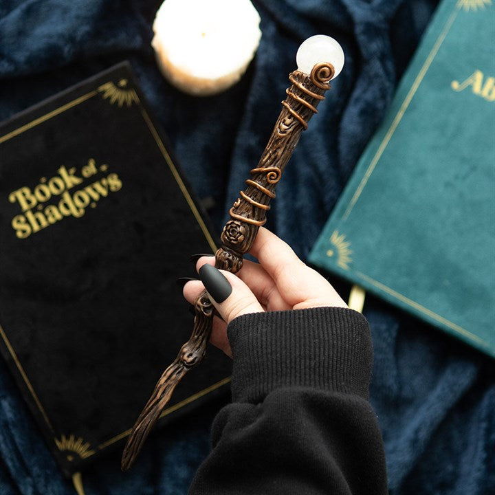 Hand holding a decorative wand with books and a candle in the background